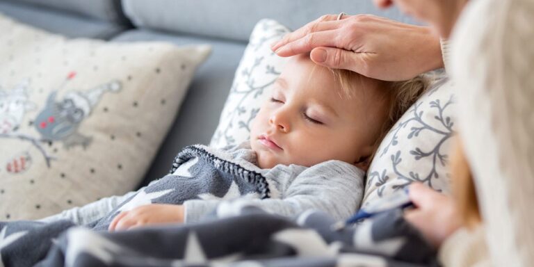 sick child laying on the couch while mom feels forehead flu in kids